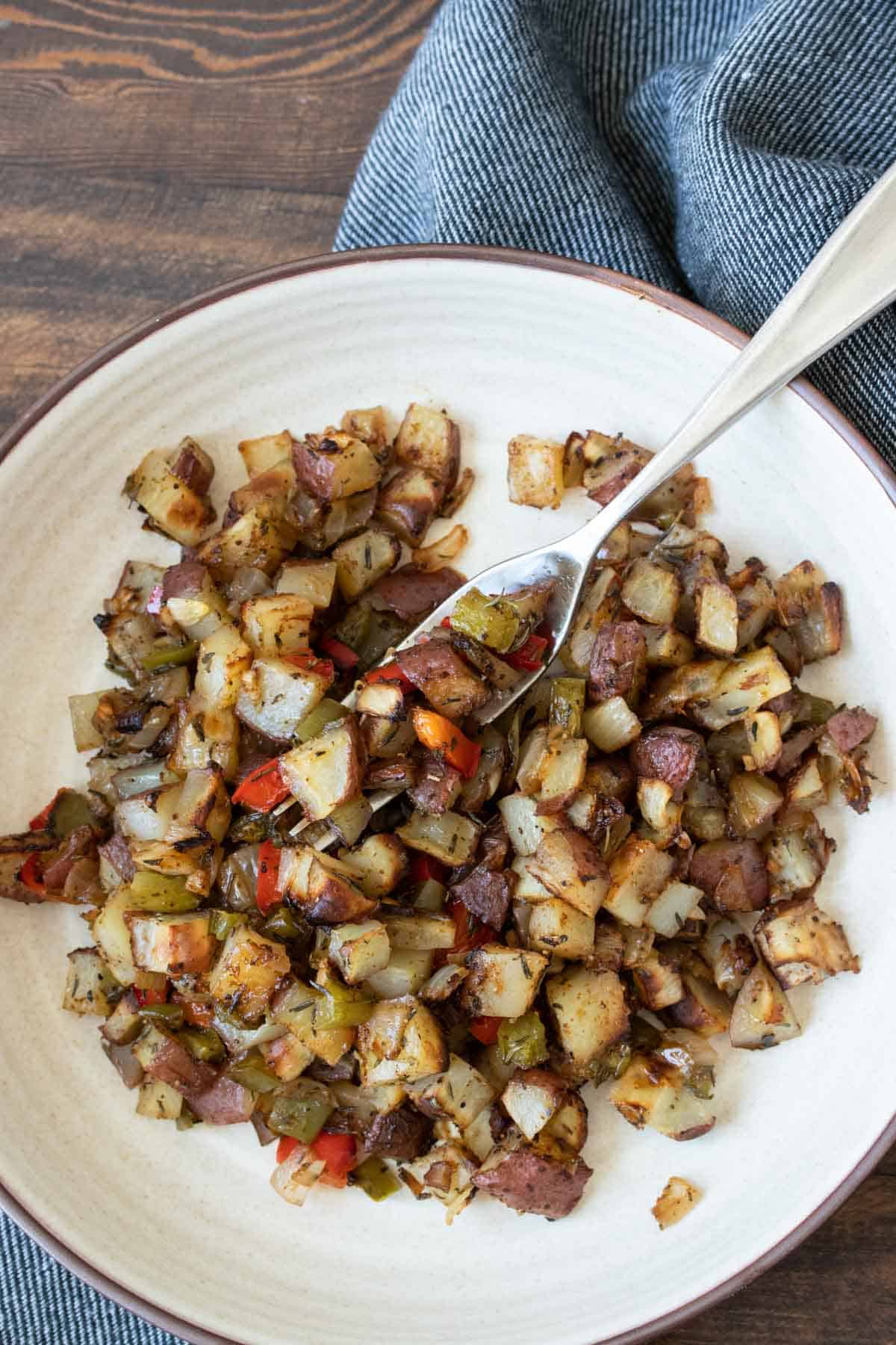 Fork getting a bite from a bowl of crispy breakfast potatoes with peppers