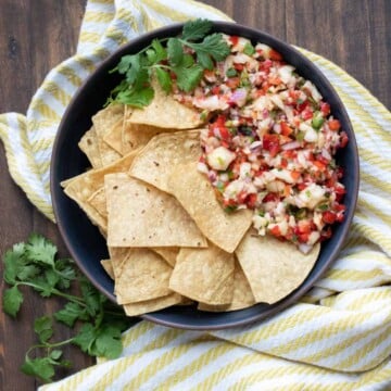 Black bowl filled with tortilla chips next to a pile of pineapple salsa