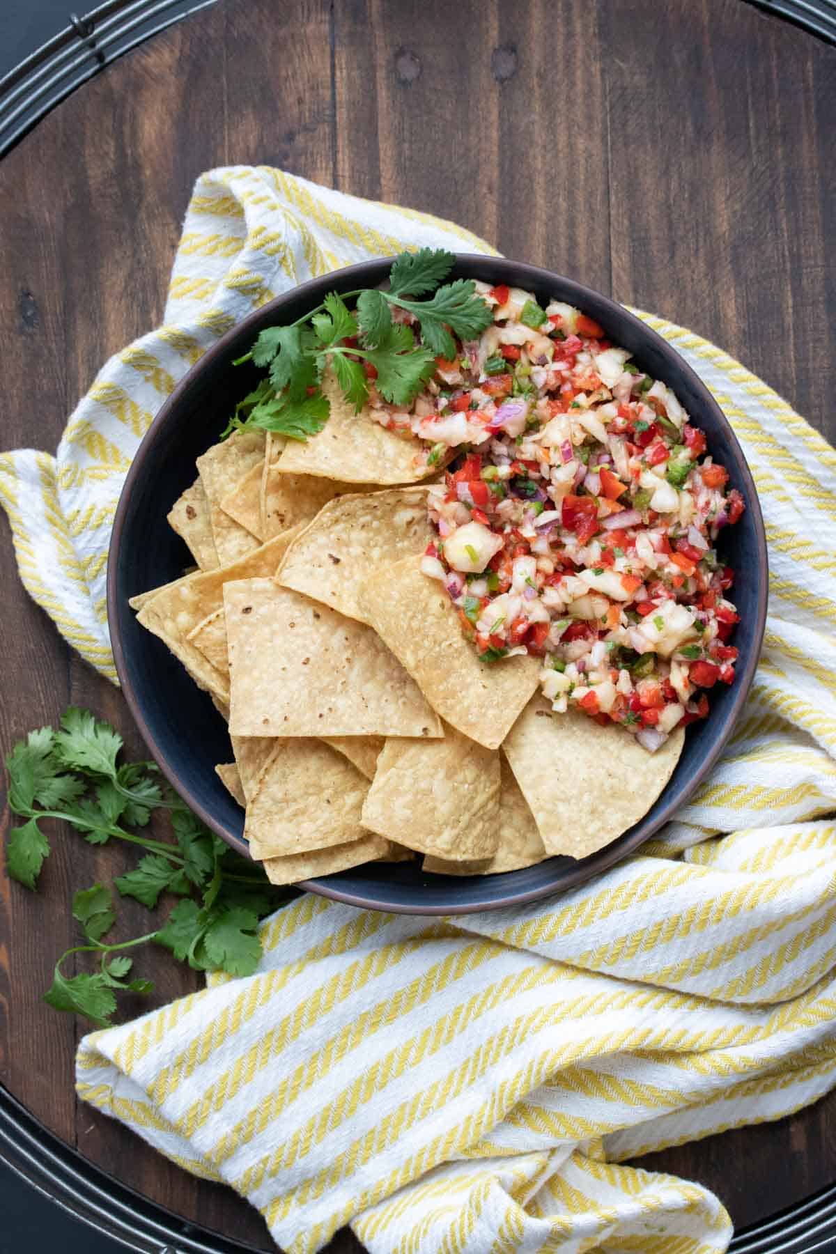 Black bowl filled with tortilla chips next to a pile of pineapple salsa