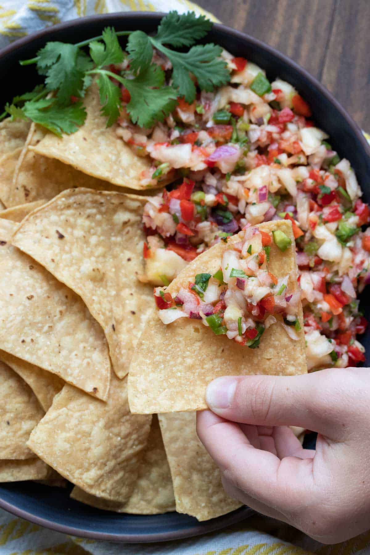 Hand taking a chip and scooping it into pineapple salsa