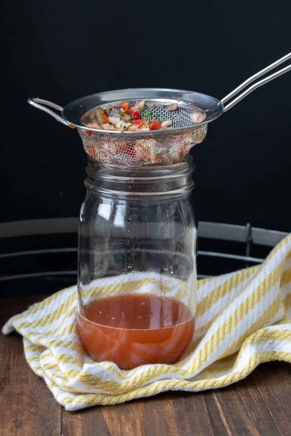 Pineapple salsa being drained through a sieve into a glass jar