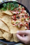 A chip being dipped into a bowl of pineapple salsa with chips next to it