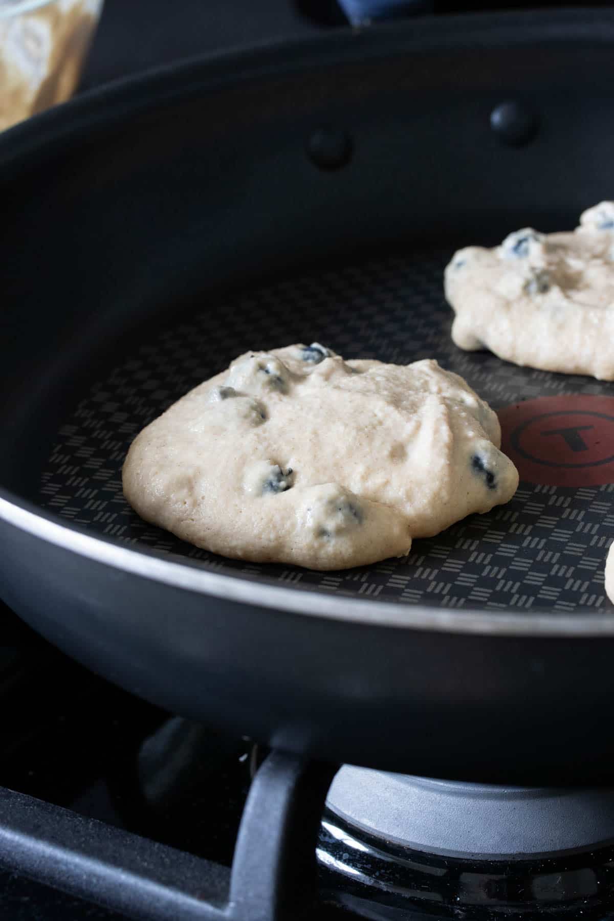 Blueberry pancakes being cooked on a black pan