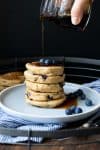 Maple syrup being drizzled over a stack of pancakes.