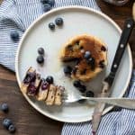 Fork with a bite of blueberry pancakes from a stack of them.