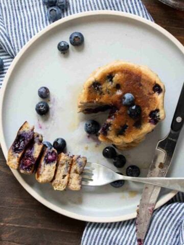 Fork with a bite of blueberry pancakes from a stack of them.