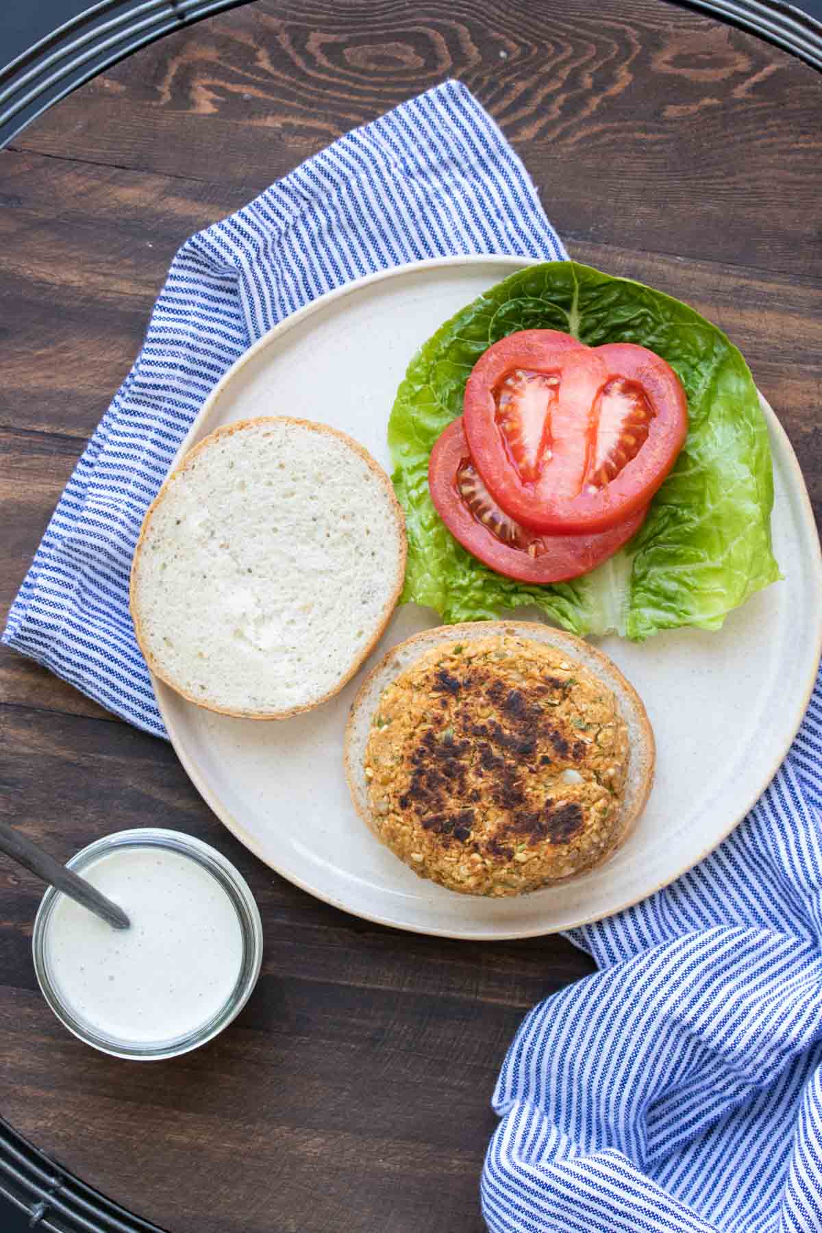Open face chickpea burger on a bun next to lettuce, tomato and sauce.