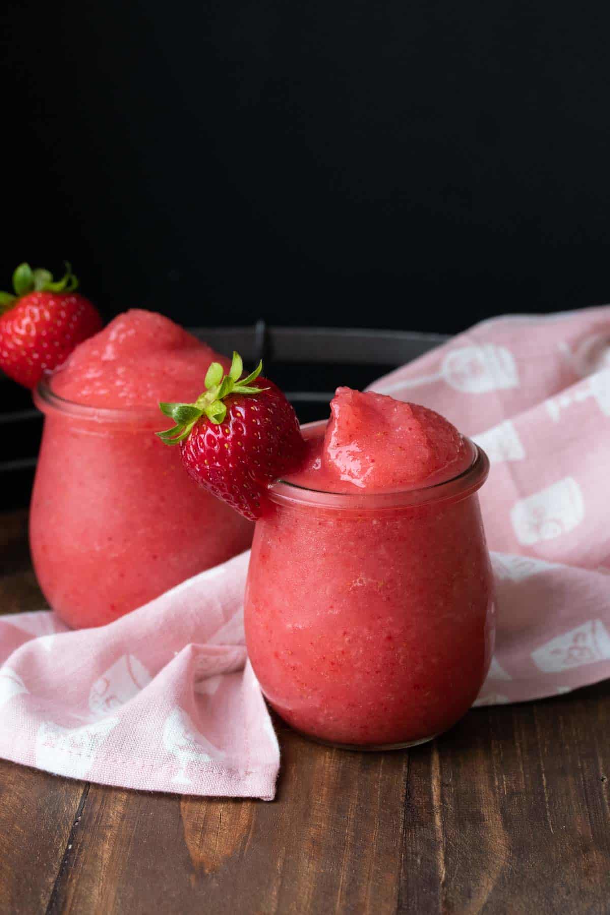 Glasses filled with bright pink blended frose recipe and a strawberry.