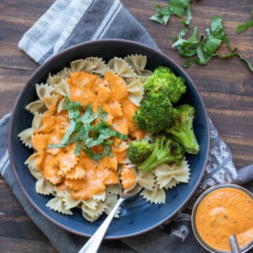 Dark blue plate with farfale pasta topped with roasted red pepper sauce and broccoli