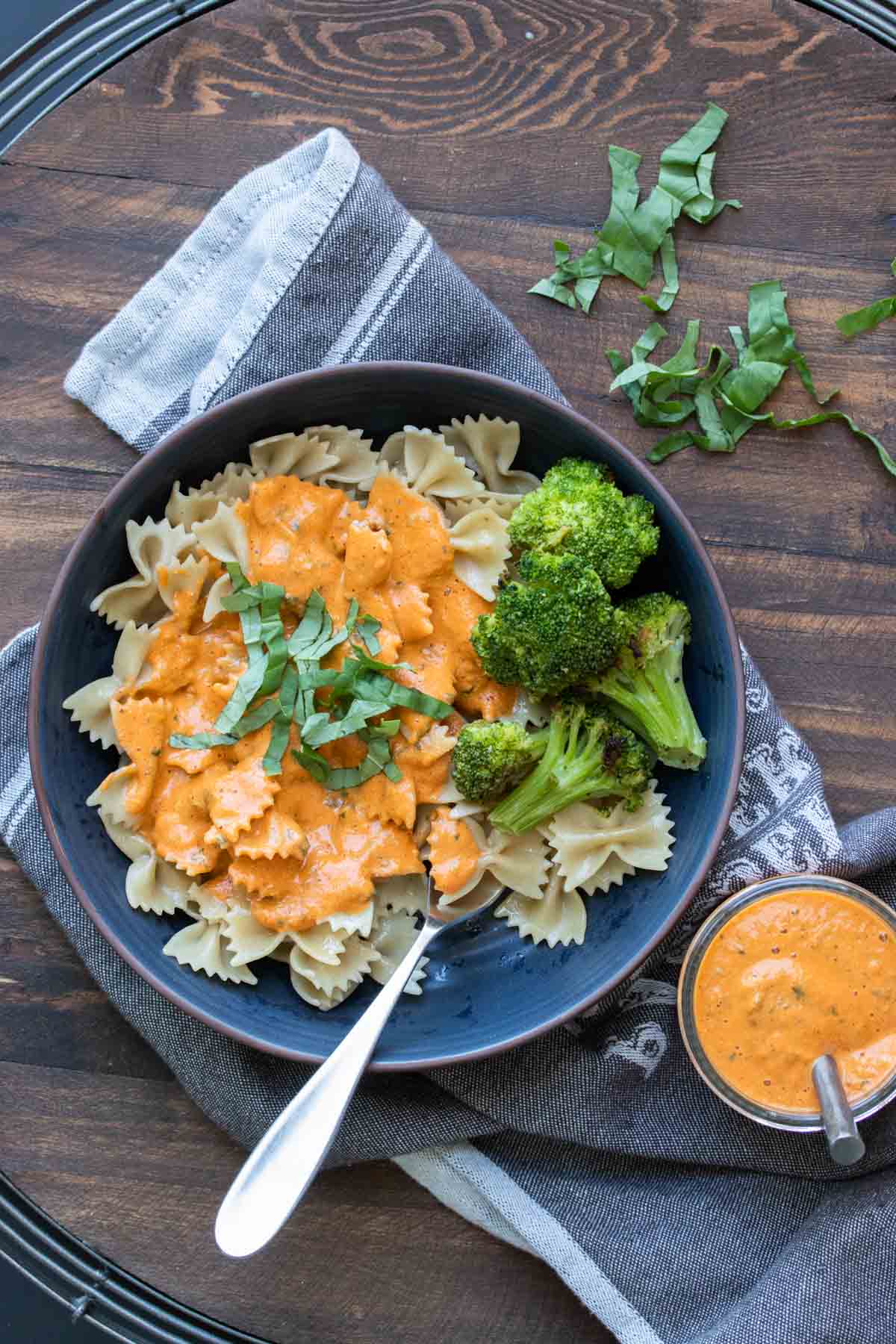 Dark blue plate with farfale pasta topped with roasted red pepper sauce and broccoli