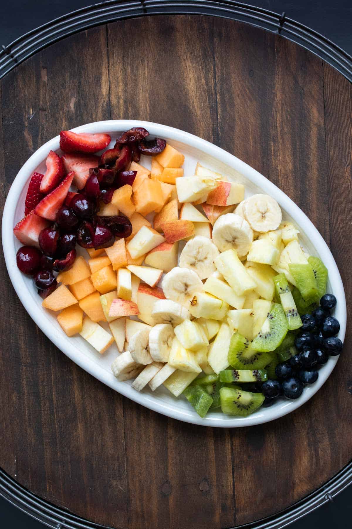 White platter with rows of different cut up fruit