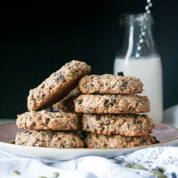 Pink plate stacked with oat breakfast cookies in front of a milk glass