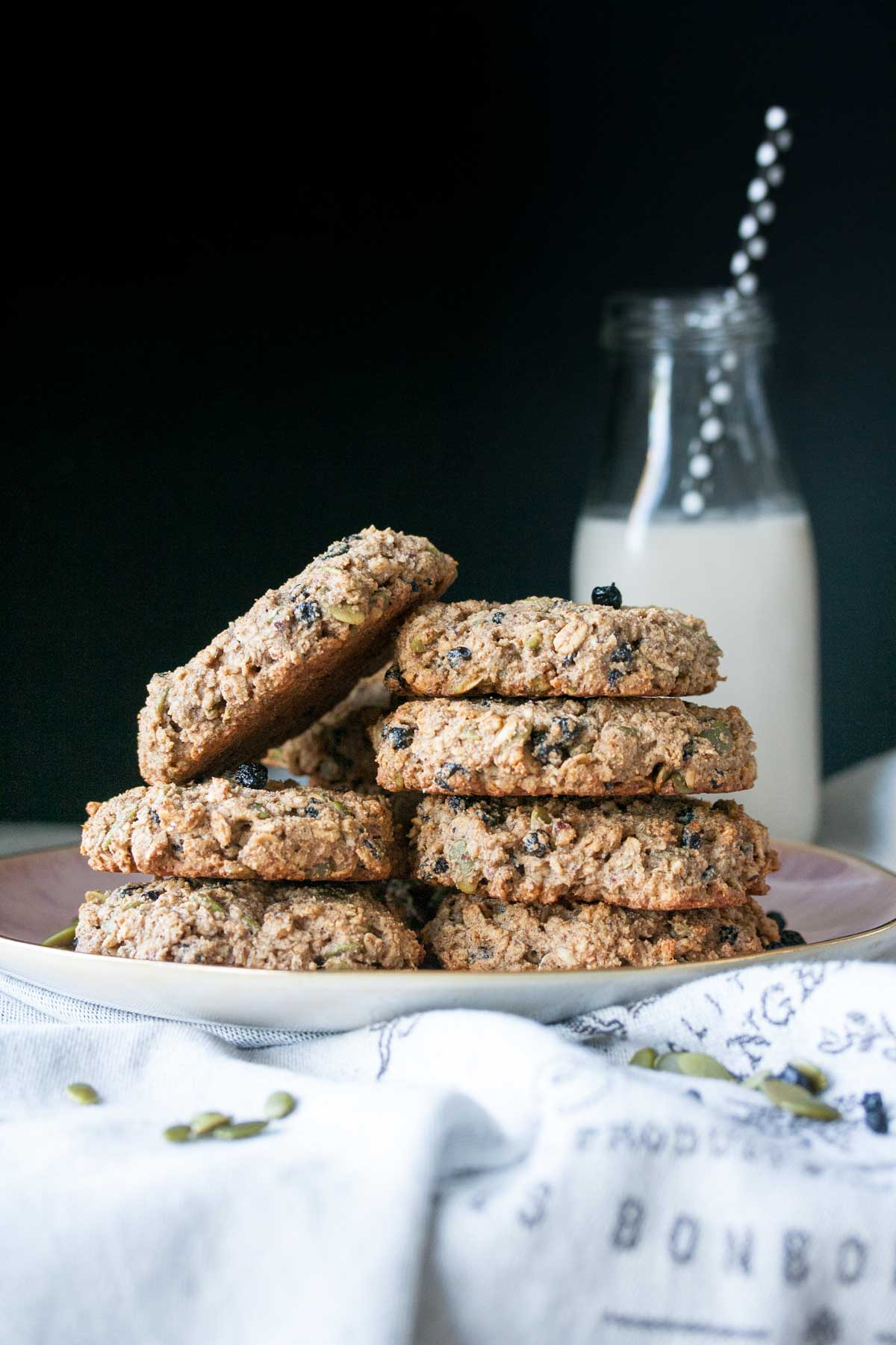 Pink plate stacked with oat breakfast cookies in front of a milk glass