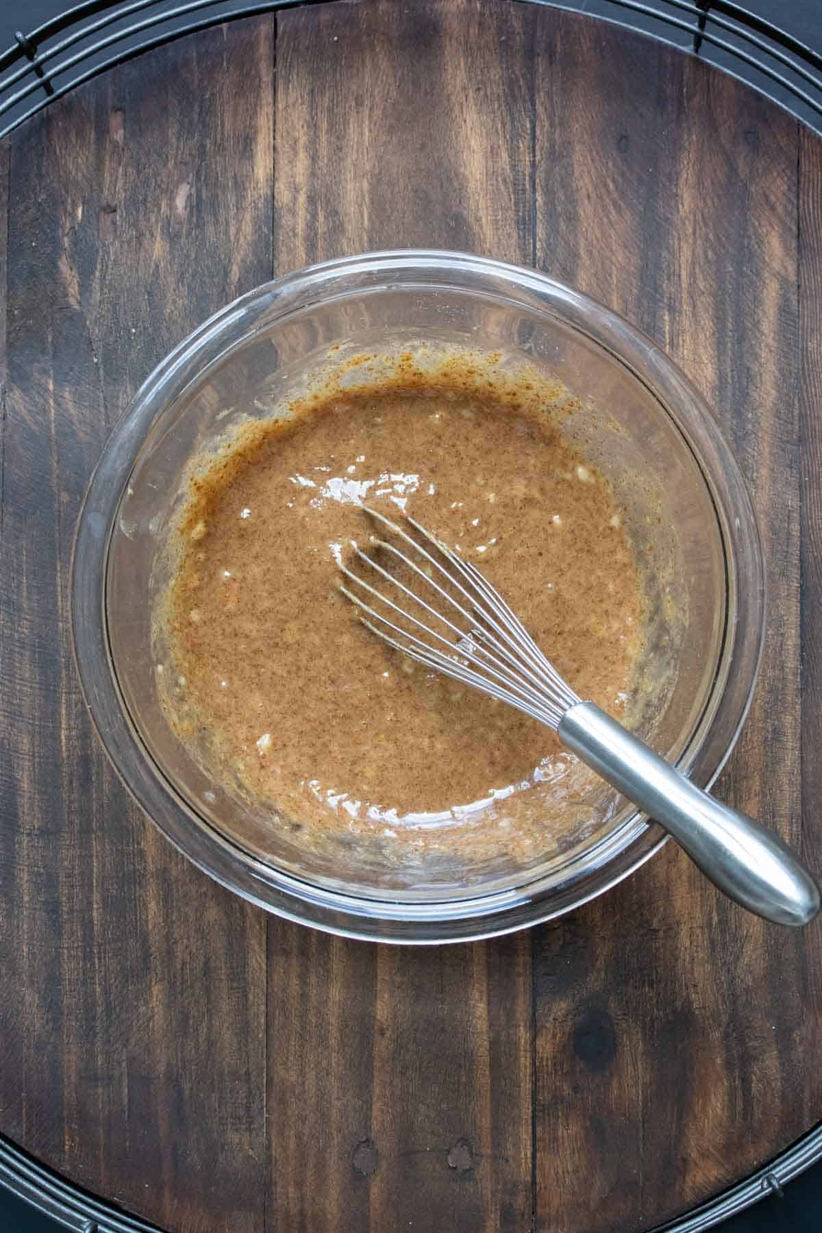 Whisk mixing tan batter in a glass bowl