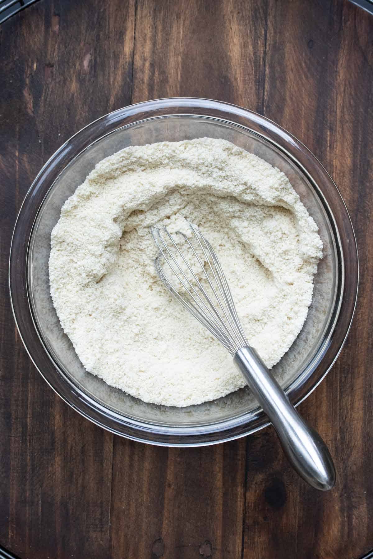 Glass bowl with flour and a whisk in it.