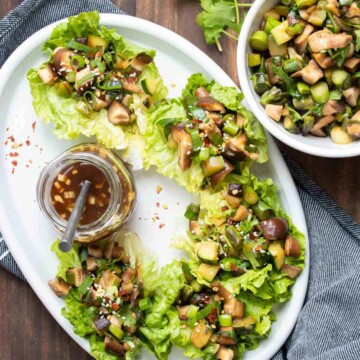 White platter with lettuce cups filled with mushroom filling and a jar of sauce