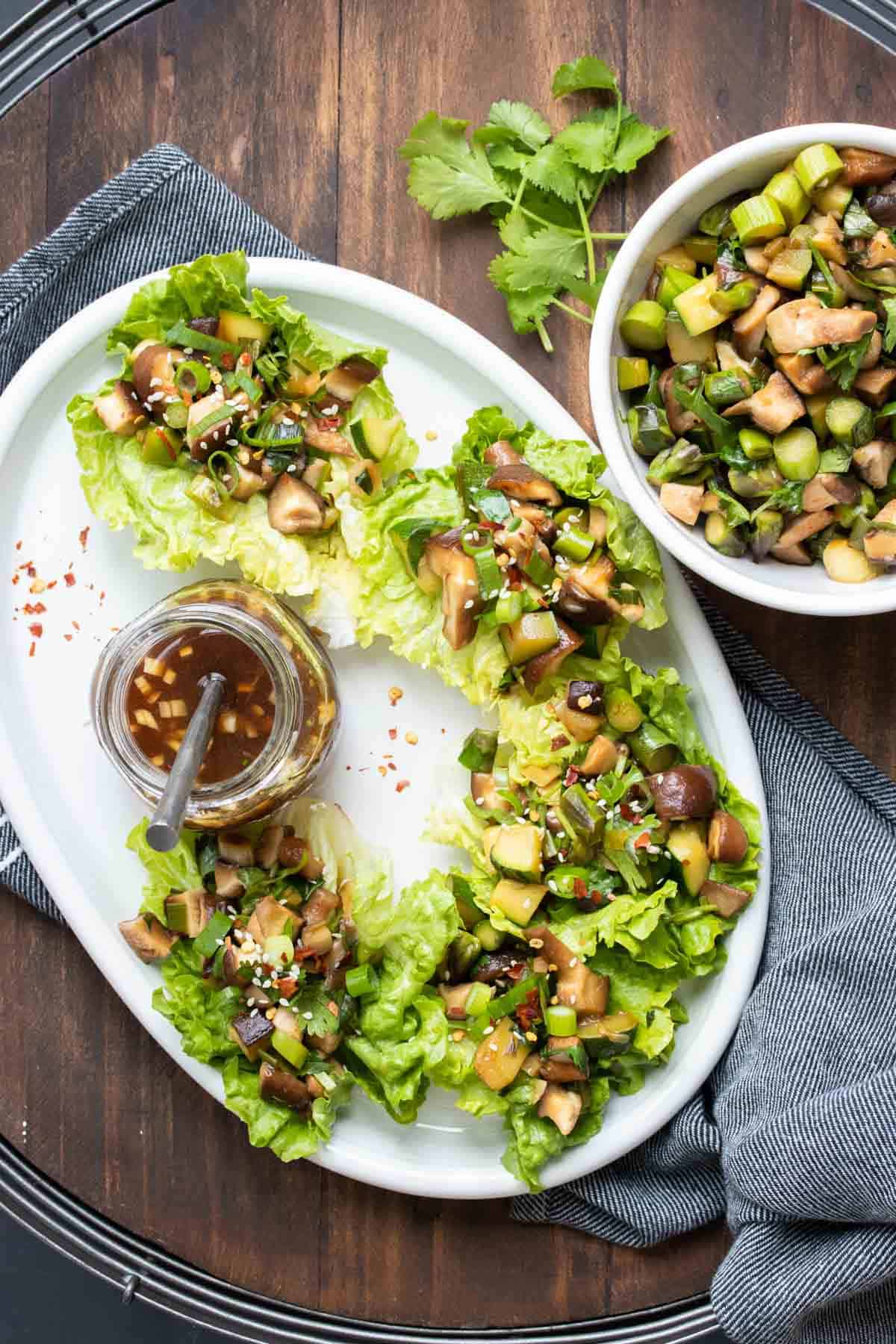 White platter with lettuce cups filled with mushroom filling and a jar of sauce