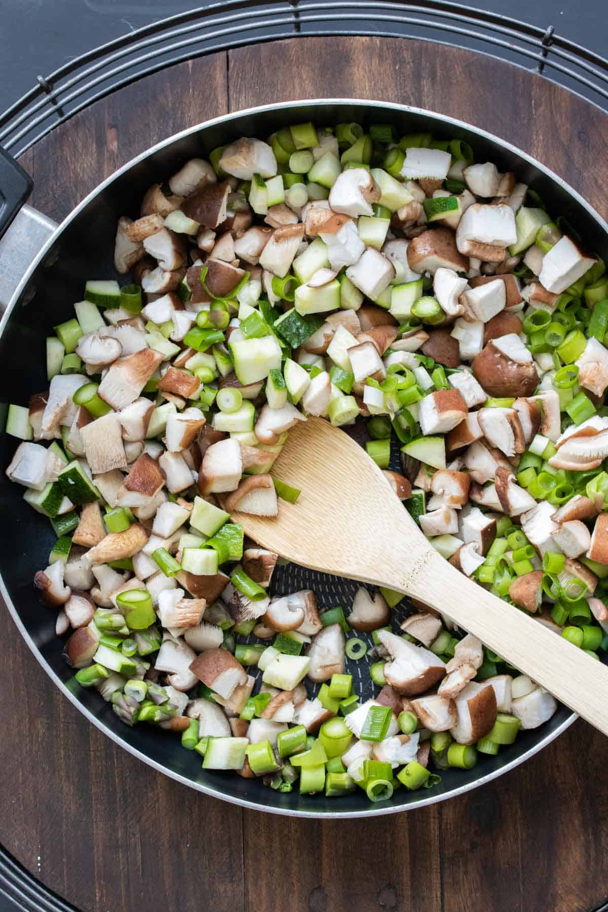 Wooden spoon mixing chopped mushrooms and asparagus in a pan