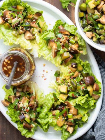 Mushroom filled lettuce wraps on a white platter with a jar of sauce