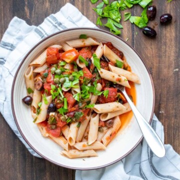 White bowl with penne pasta mixed with puttanesca sauce and parsley
