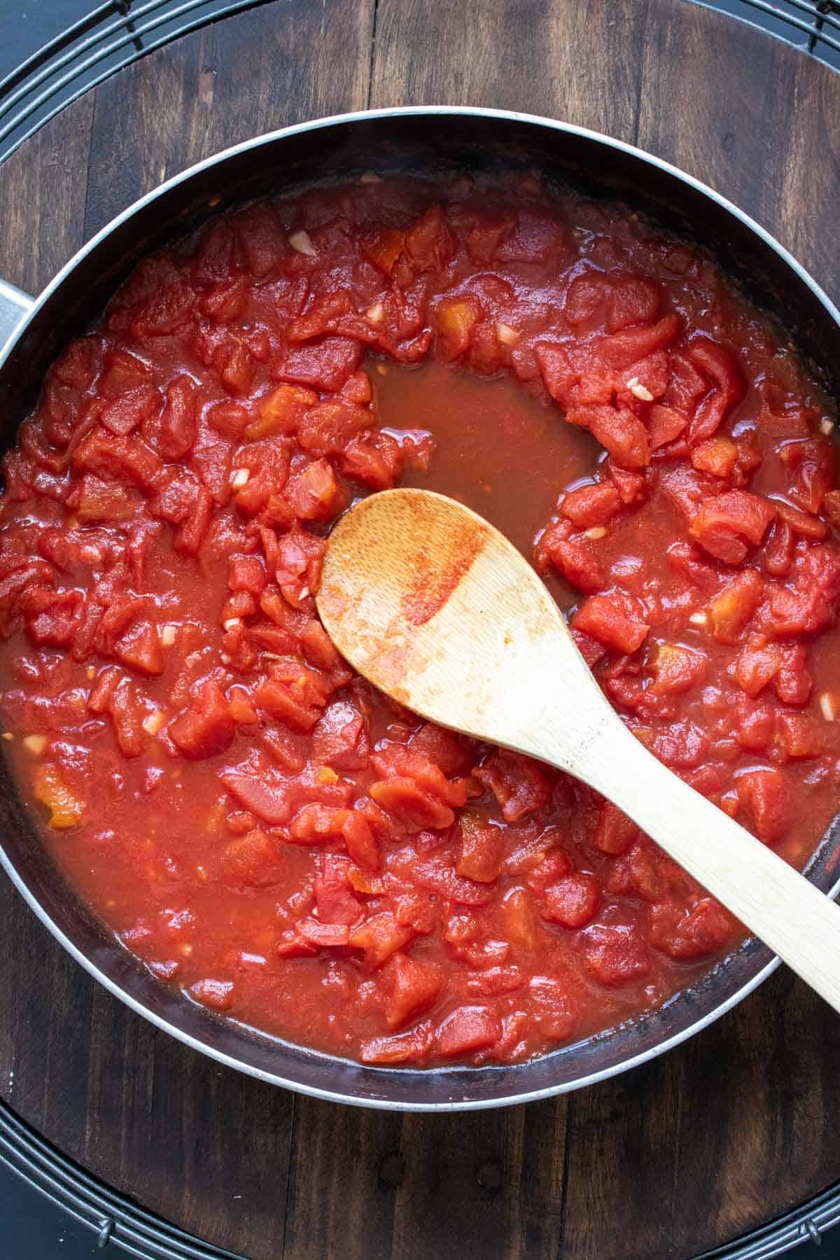 Wooden spoon mixing tomato sauce in a pan.