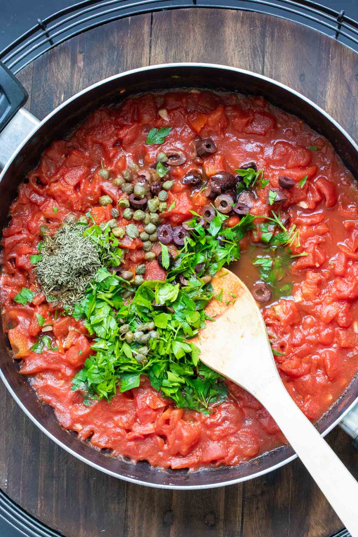 Tomato sauce with parsley, herbs and olives in a pan.