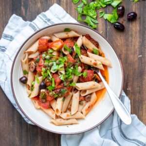 Fork in a white bowl with pasta and puttanesca sauce