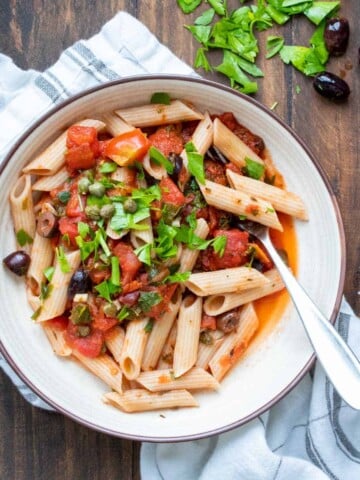 Fork in a white bowl with pasta and puttanesca sauce