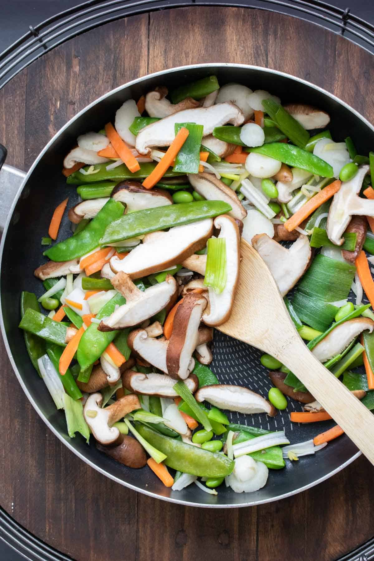 Wooden spoon sautéing veggies in a pan