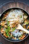 Noodles and veggies mixing with a brown sauce in a pan