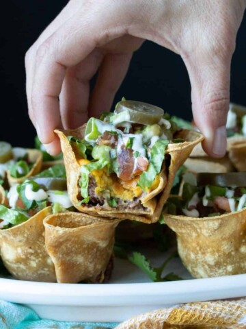 A photo of tortilla shaped like cups with layers of filling on a plate and a hand grabbing one