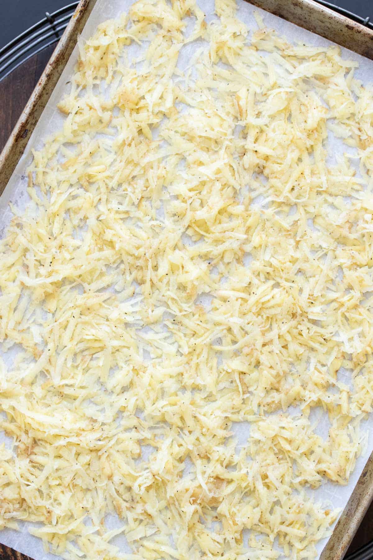 Shredded raw potato spread out on a parchment lined baking sheet
