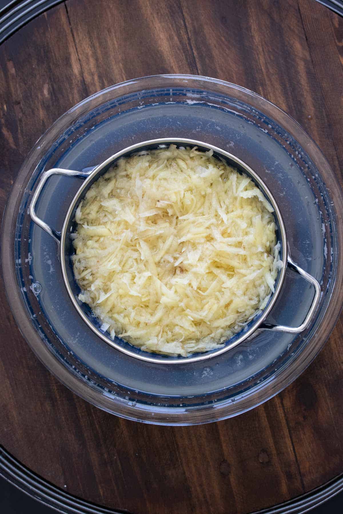 Shredded raw potato in a colander in a bowl of water