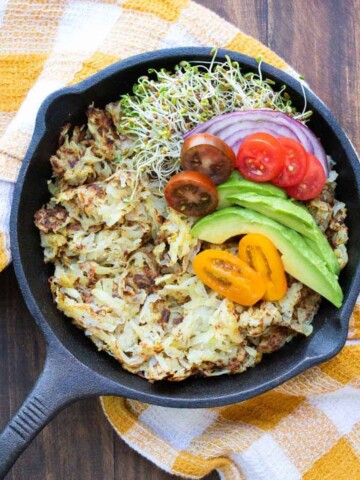 Black skillet filled with hashbrowns and topped with veggies