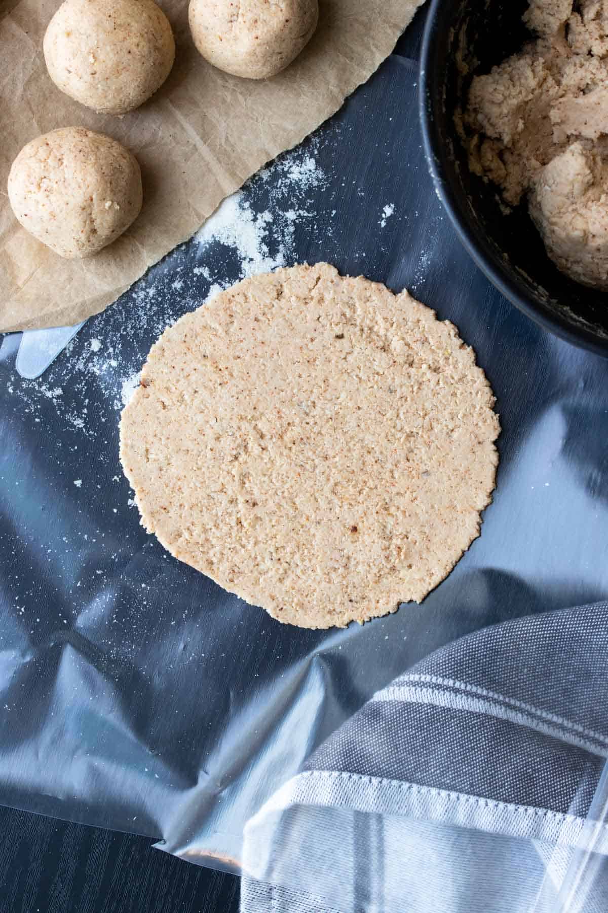 Raw homemade corn tortilla on a black table next to balls of dough