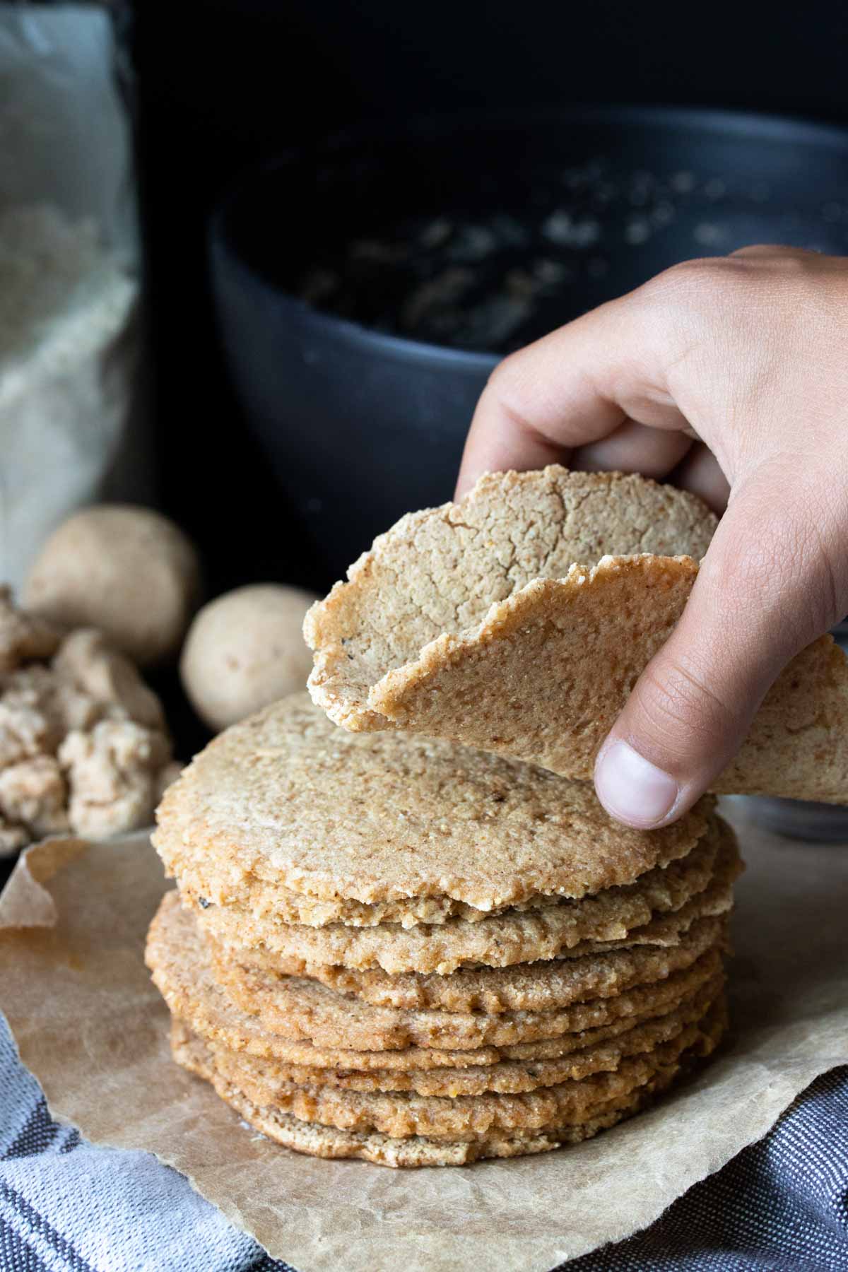 Hand holding a cooked corn tortillas over a pile of them