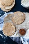 Two homemade corn tortillas on a piece of parchment and one has a bite from it