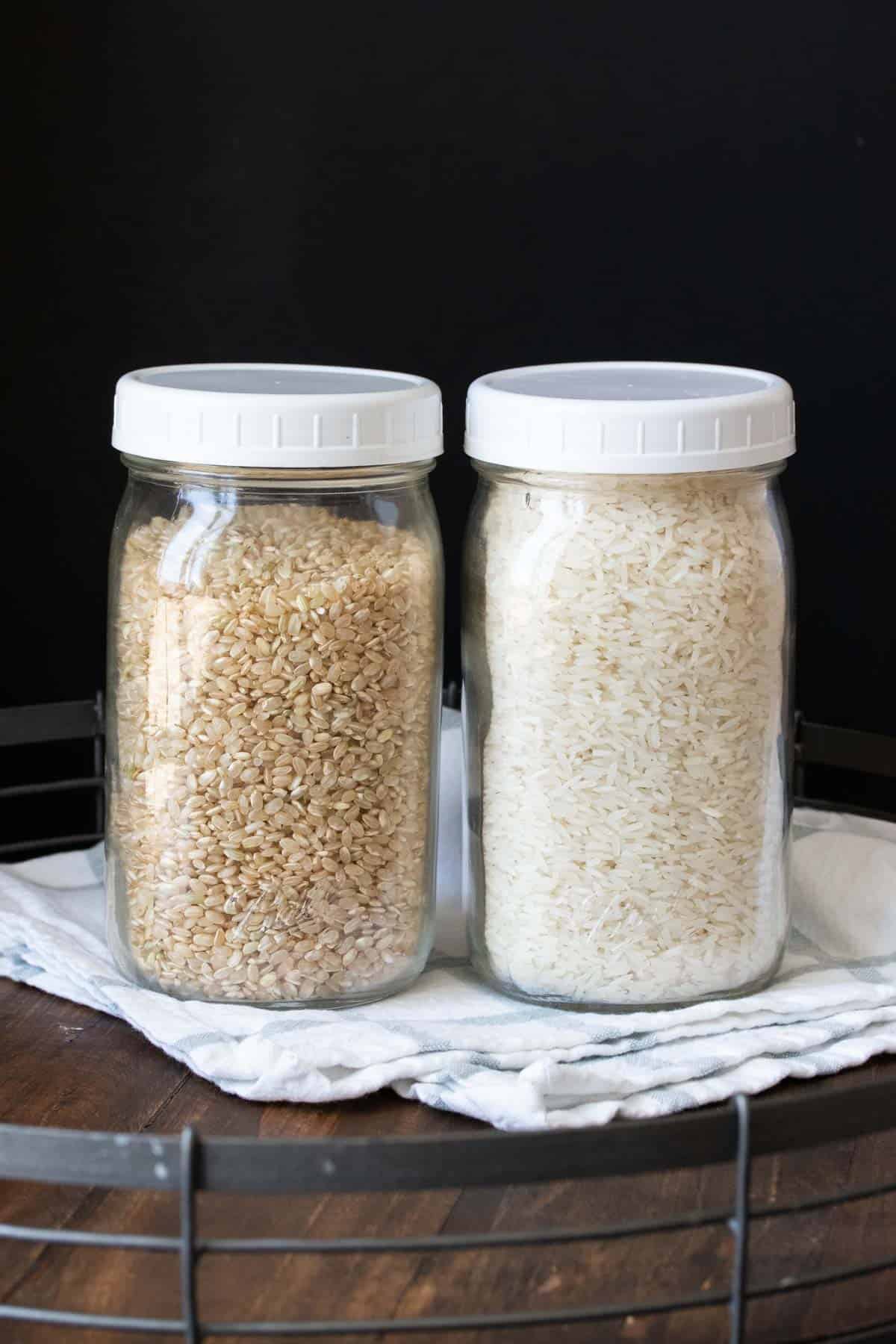 Two glass jars with white lids and different colors of rice inside