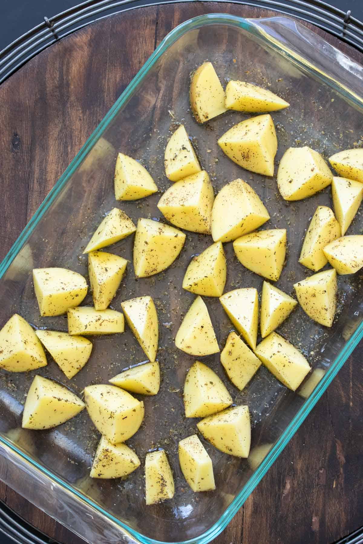 Glass baking dish with cut potatoes and oregano.