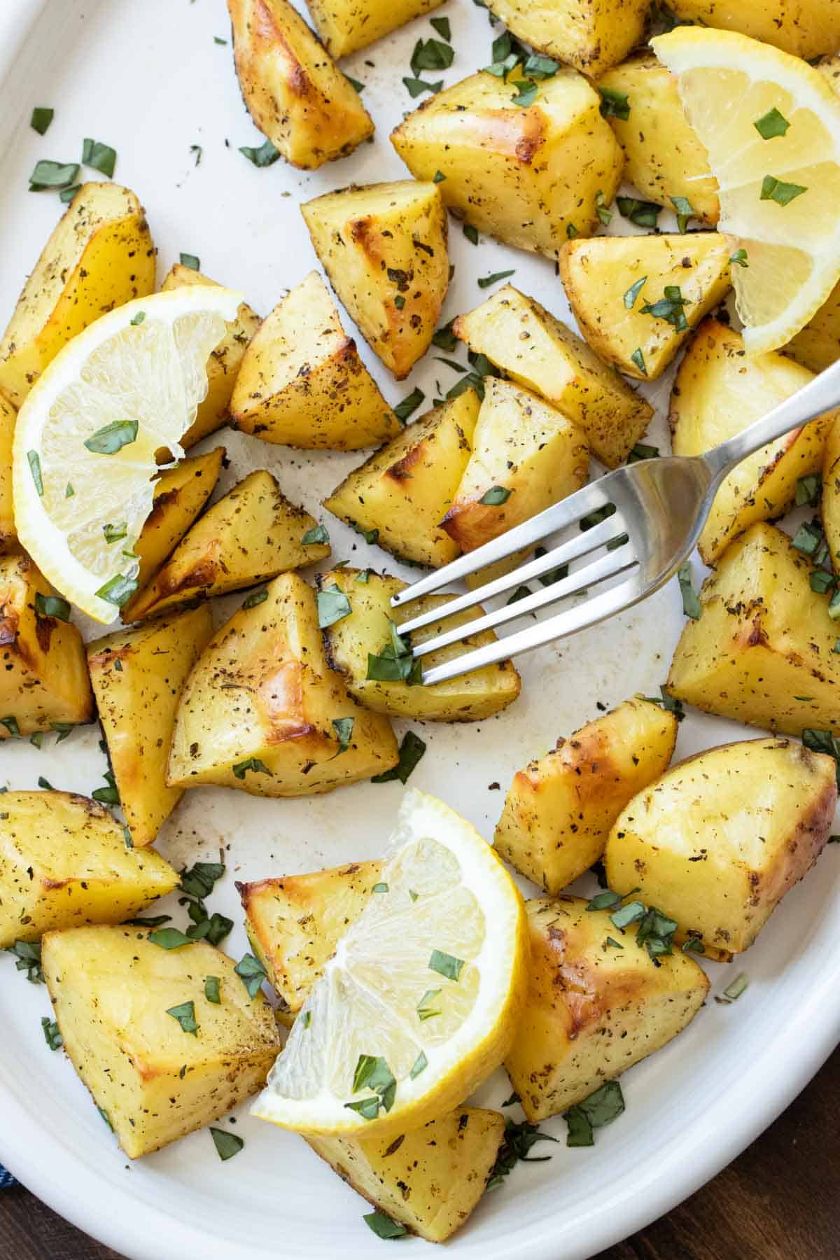 Fork getting a bite of an oven roasted oregano potato from a platter.