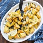 Black spatula getting oven roasted potatoes from a white platter.