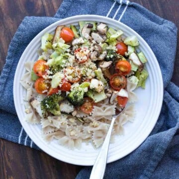 White plate with roasted veggies and pasta sprinkled with parmesan cheese