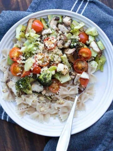 A fork in a pasta bowl filled with a roasted veggie and pasta dinner