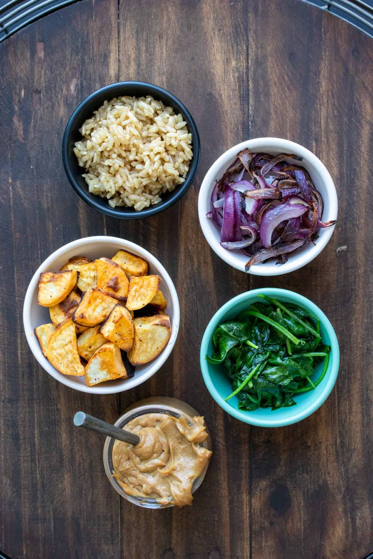 Bowls with veggies, rice and a jar with sauce on a wooden table