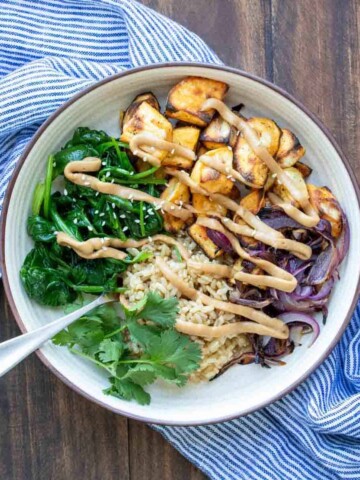 Buddha bowl with spinach, potatoes, rice and onion drizzled with sauce