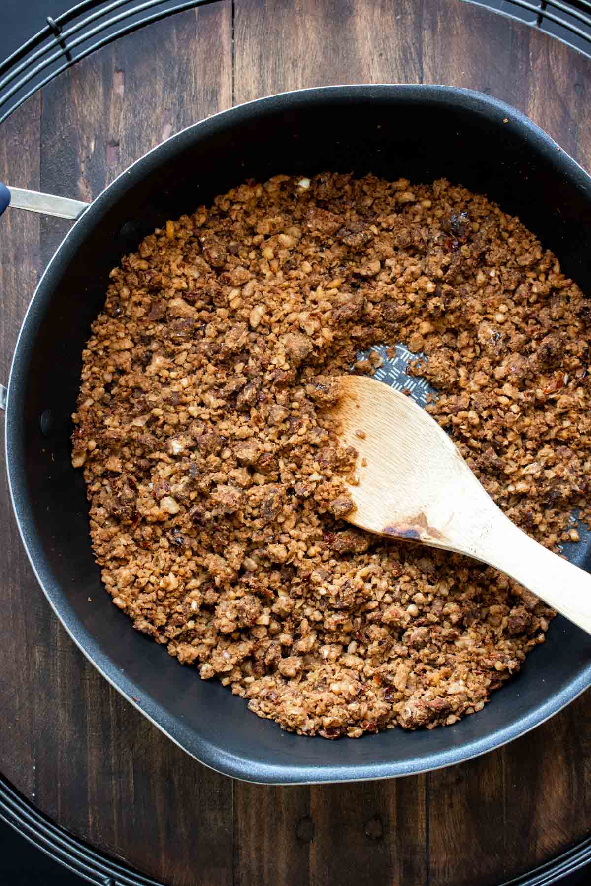 Wooden spoon sautéing vegan chorizo crumbles in a pan