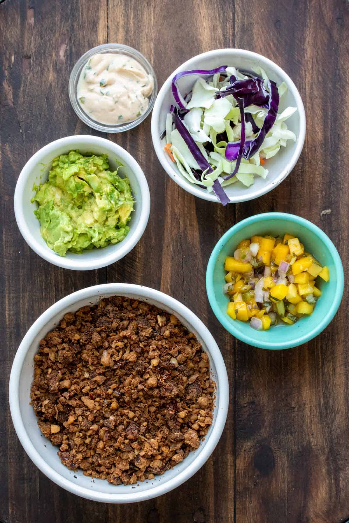 Five bowls on a wooden surface filled with ingredients for chorizo tacos