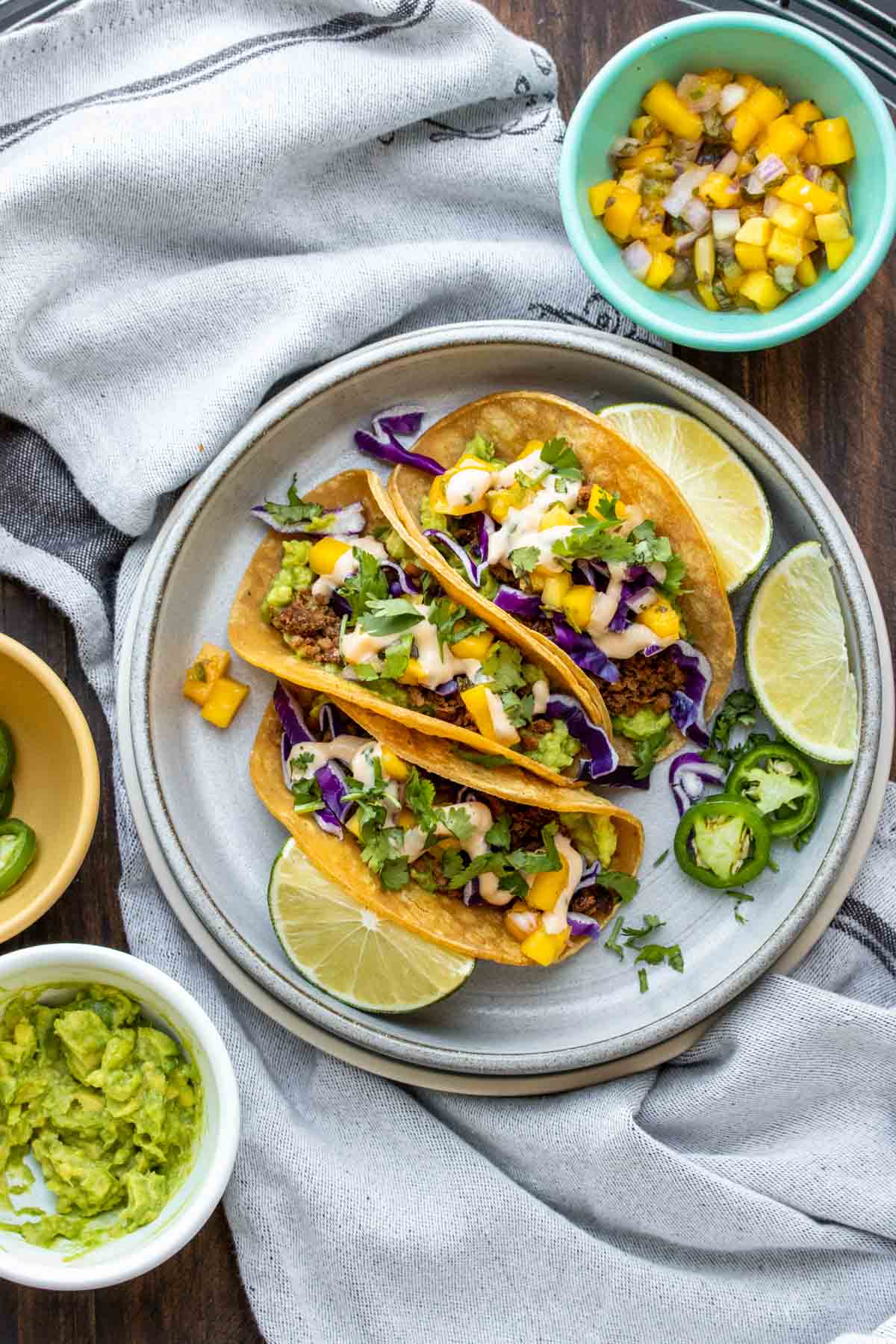 Grey plate with three vegan chorizo tacos topped with cabbage, avocado and salsa