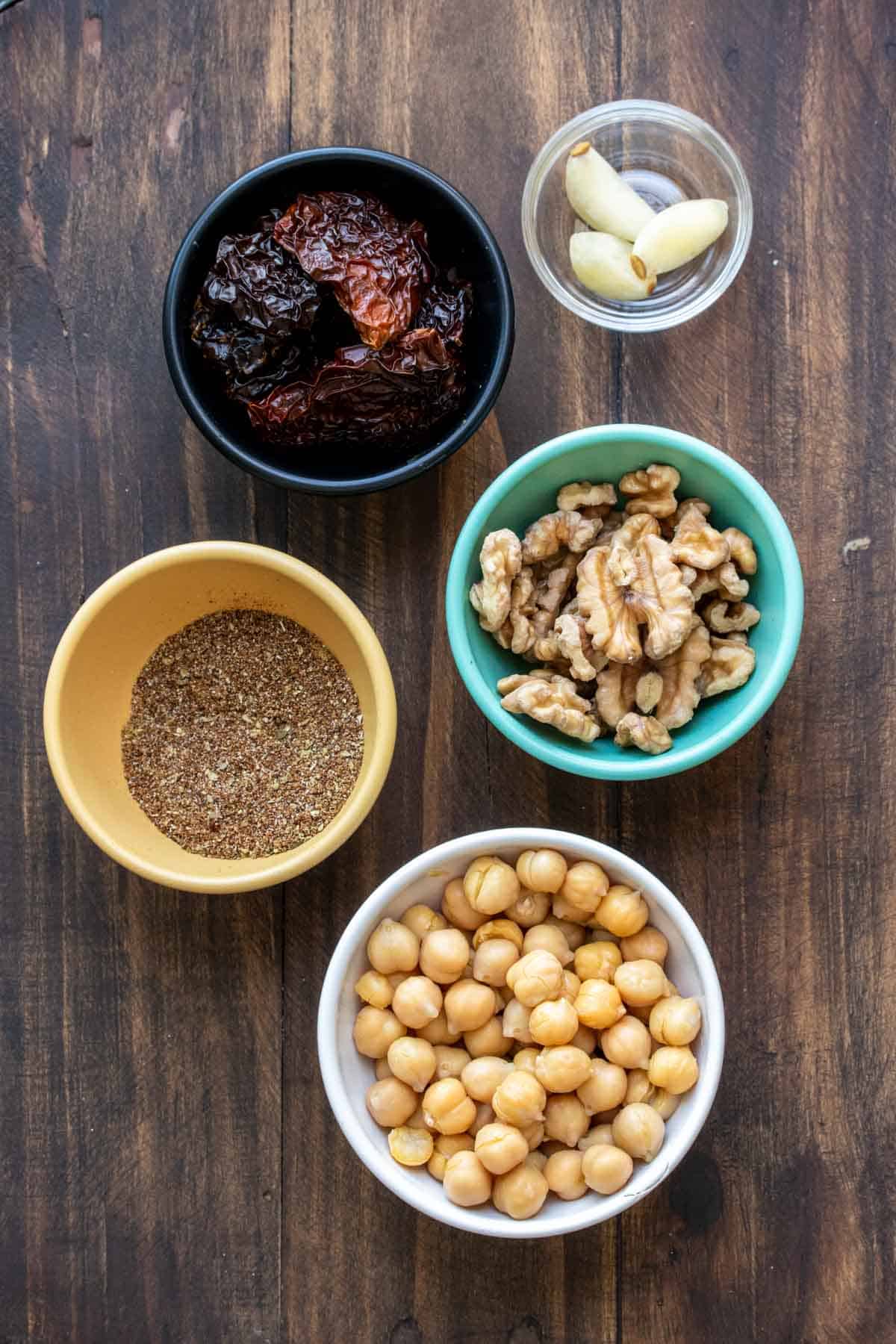 Five bowls with ingredients to make a vegan chorizo crumble on a wooden surface