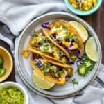 Grey plate with three vegan chorizo tacos surrounded by bowls of taco ingredients.